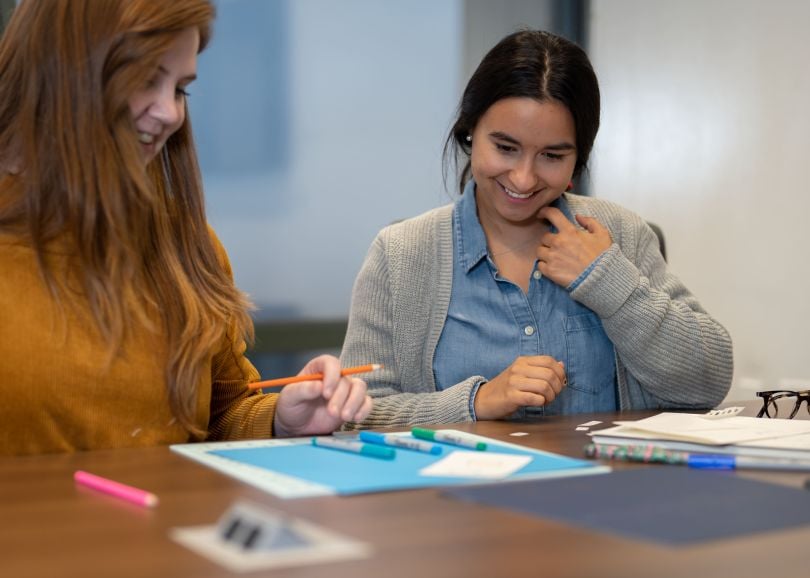 Two women of Motorola sitting at a desk, collaborating over some papers and smiling.