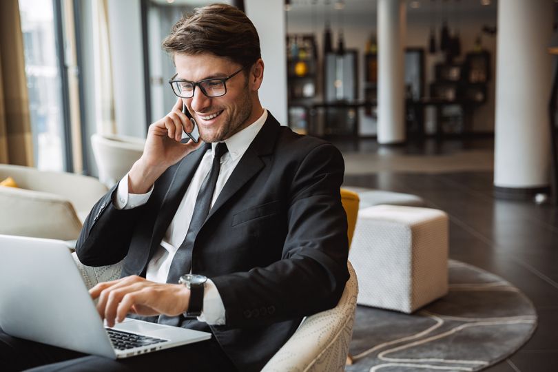 A businessman wearing a black suit using laptop computer and talking on a mobile phone