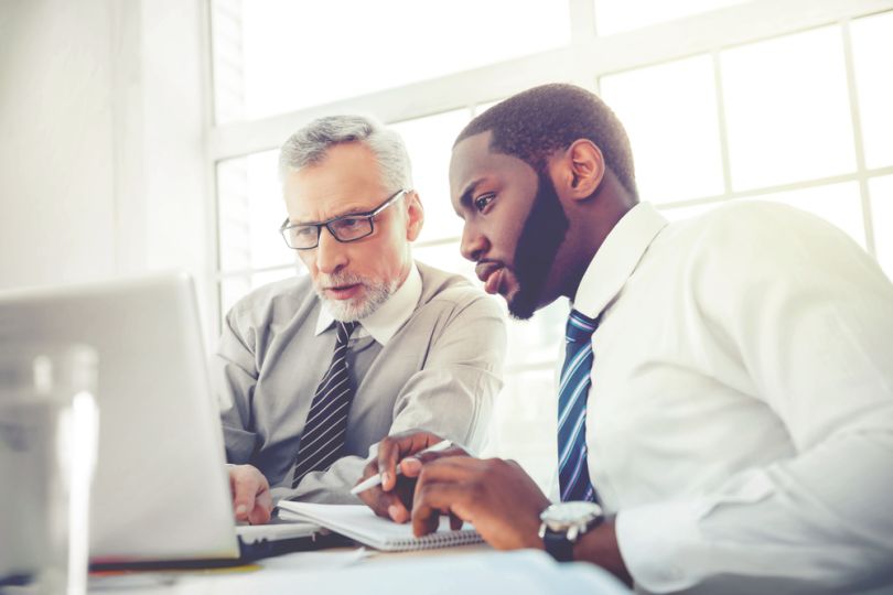 An employee and a manager sit side-by-side looking at a laptop.
