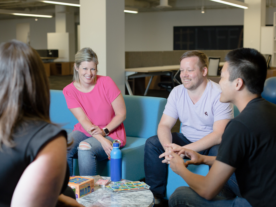 Lauren sits on a blue sofa smiling with coworkers