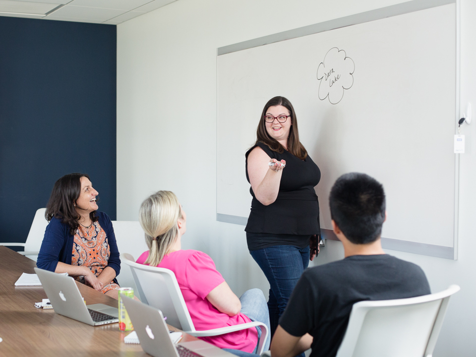 Val stands in front of a whiteboard, surrounded by coworkers