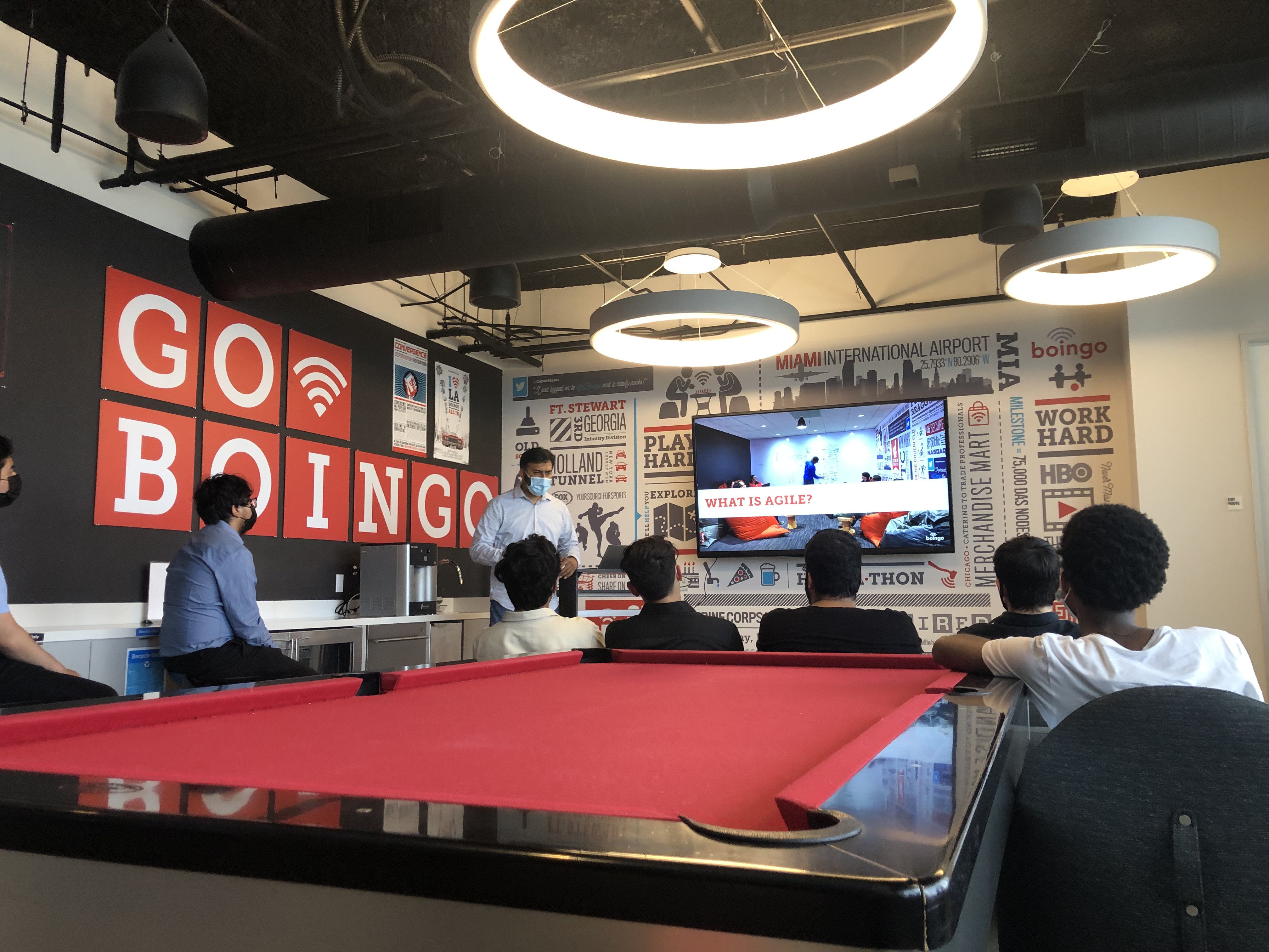 A group of Boingo employees sit around a pool table for a presentation