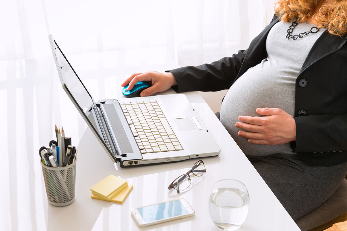 Young pregnant business woman sitting at a desk working on a laptop