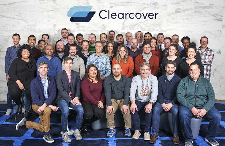 Clearcover team in office posing for photo below their logo