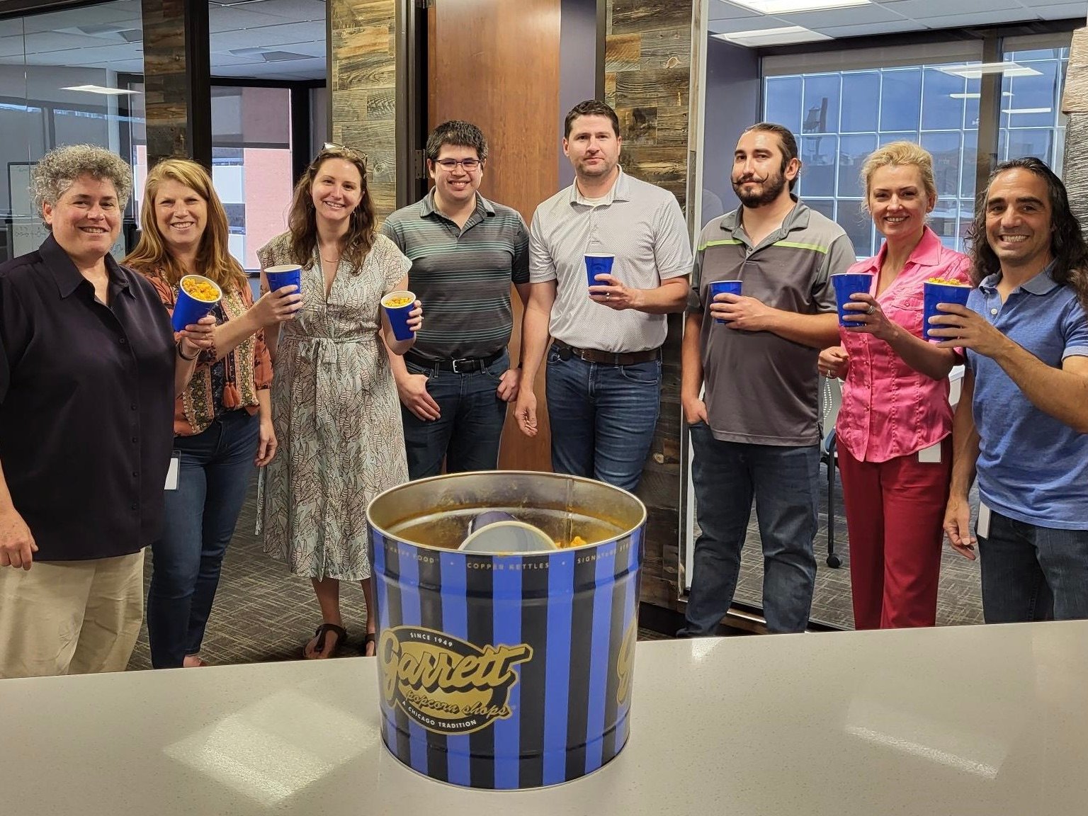A group of Invenergy employees smile and pose in front of a half-eaten tin of Garrett brand popcorn.