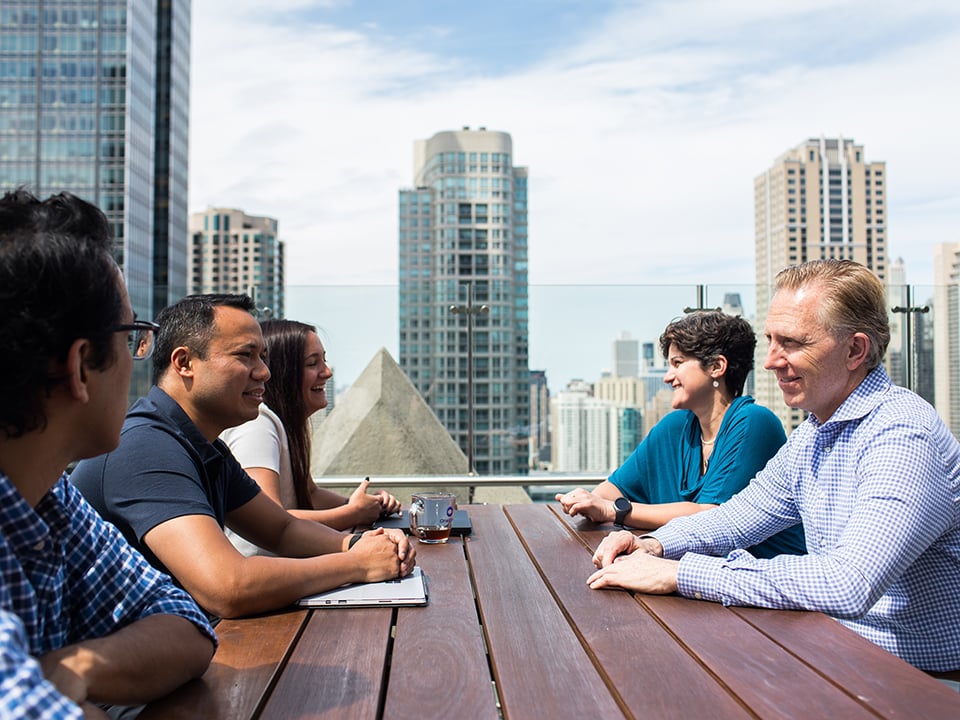 Scott Clements sits at a table with employees on OneSpan's rooftop 