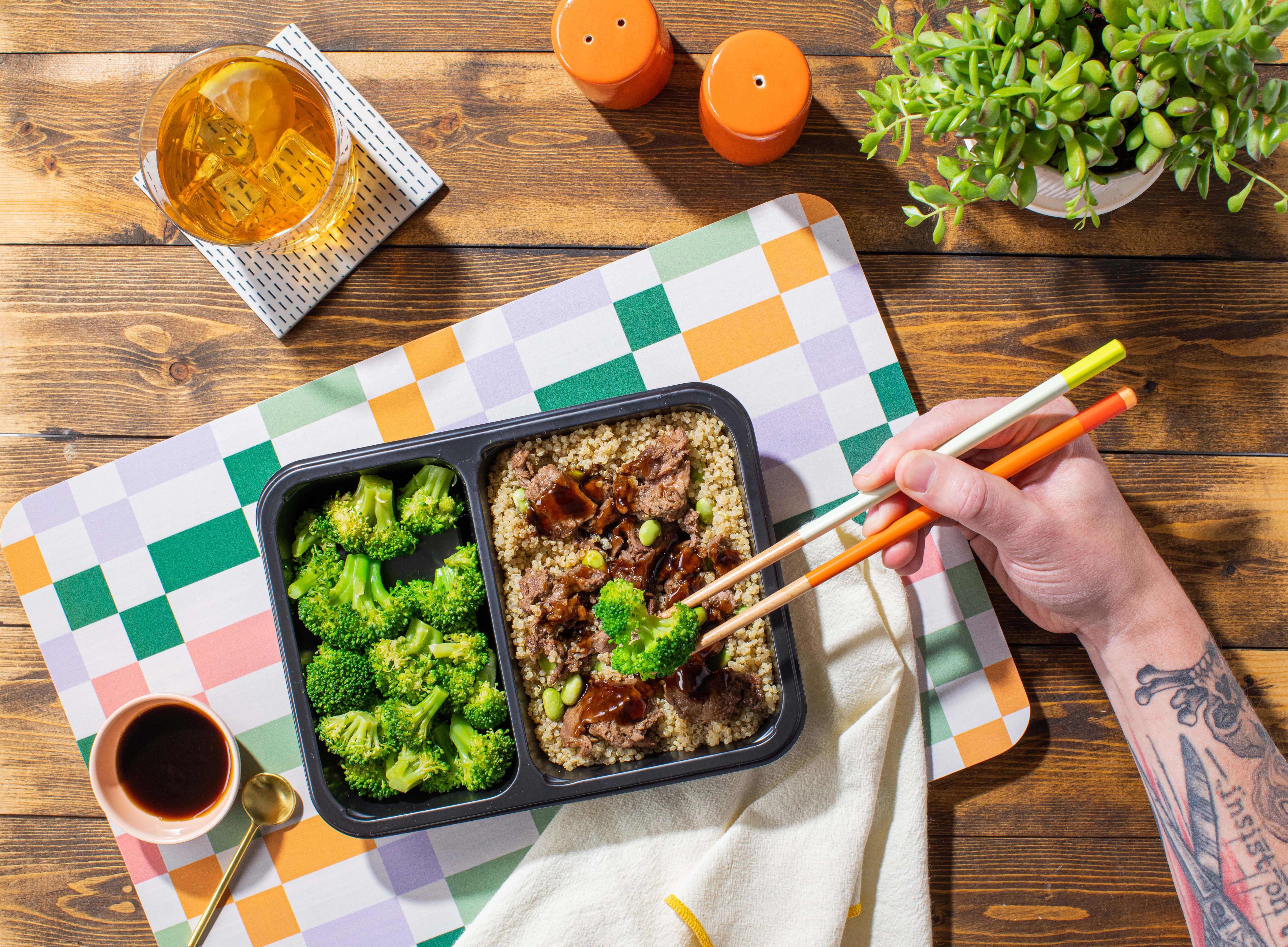 The Tempo Black Pepper Beef dish on a table, with a hand holding chopsticks, ready to eat