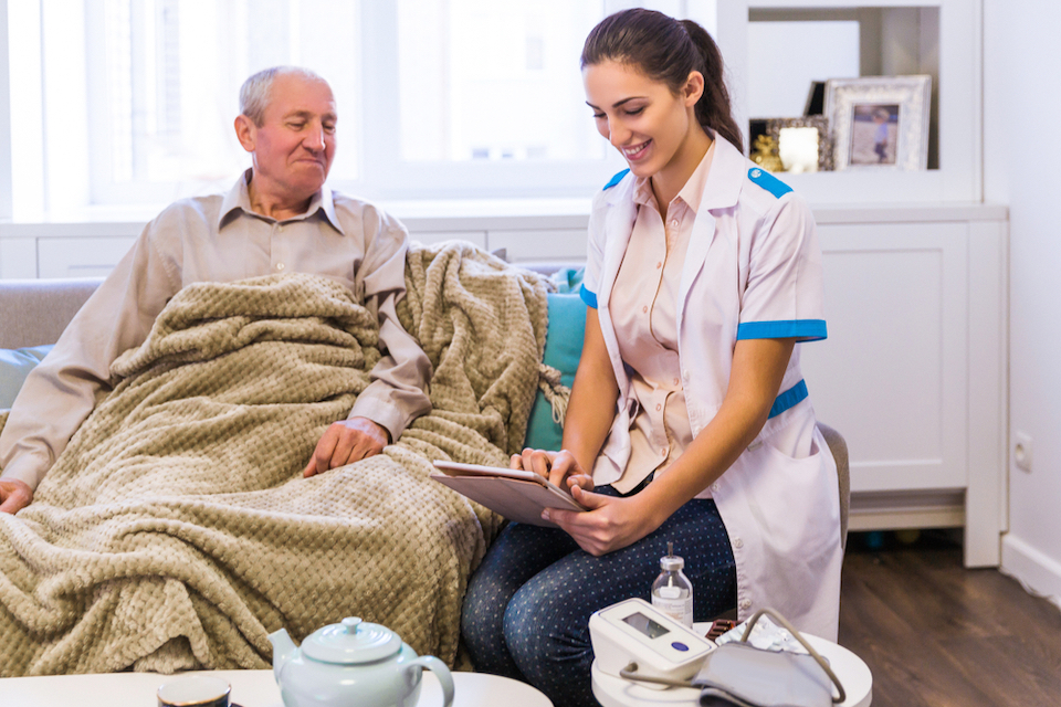 Female nurse smiles as she works on tablet with nursing home patient