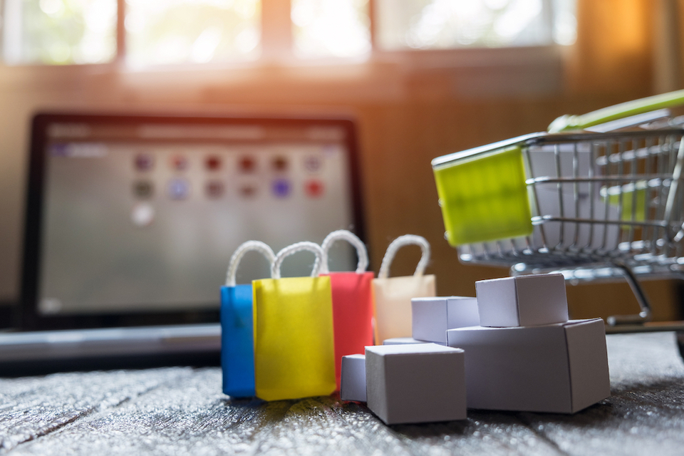 Miniature shopping cart and shopping basket placed in front of a laptop