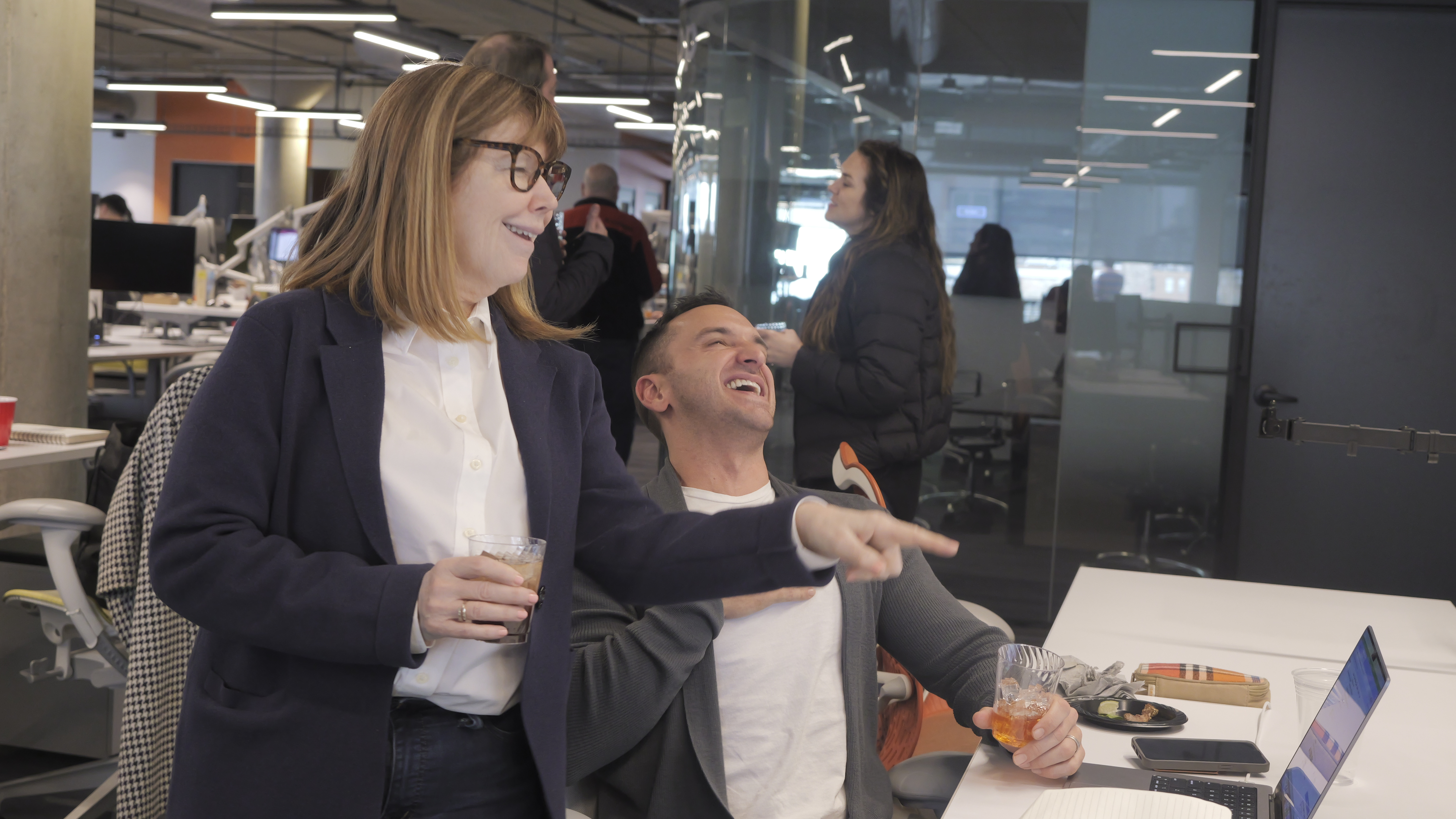 Woman pointing at screen making a joke, her colleague laughing