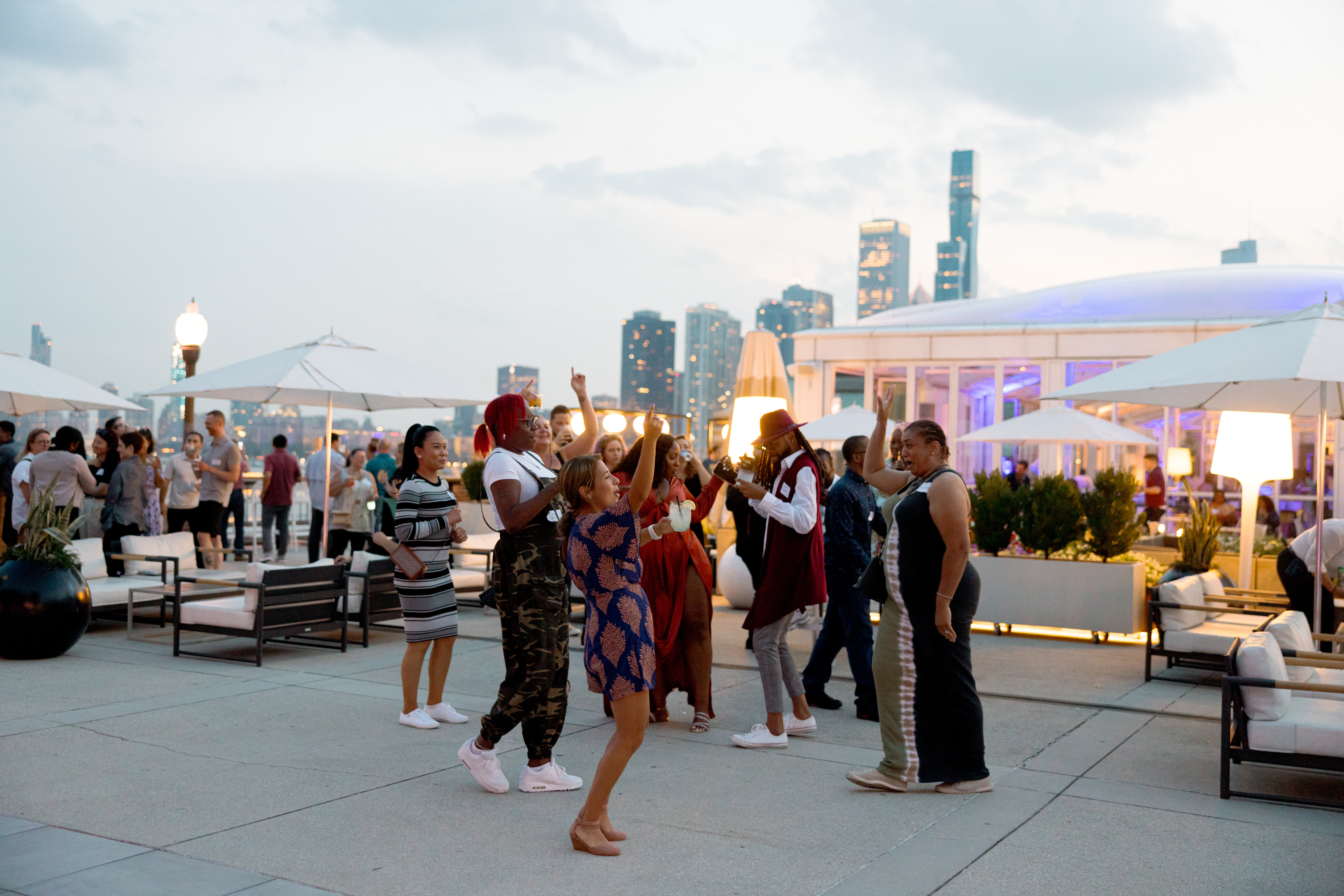 OppFi team members cheer in outdoor rooftop setting with Chicago skyline in the background at dusk during a Thrive Where You Work Week event. 