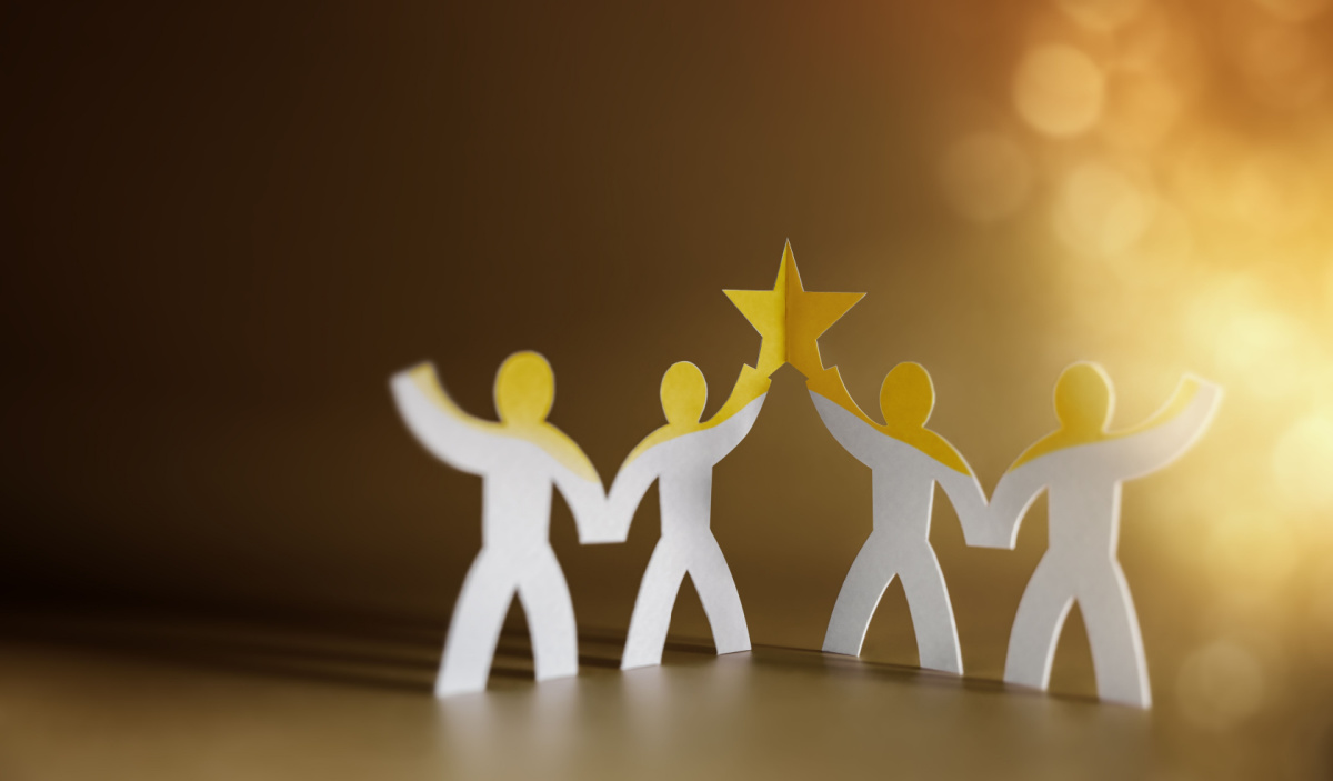Paper figures holding up a star together against a warm, glowing background.