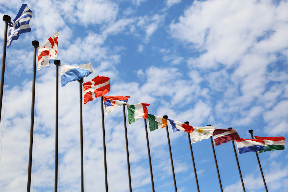 Flags from numerous countries pictured with cloudy, blue sky in background