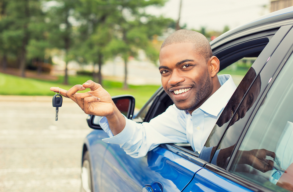 Man in car leaning out of window smiling and holding car keys