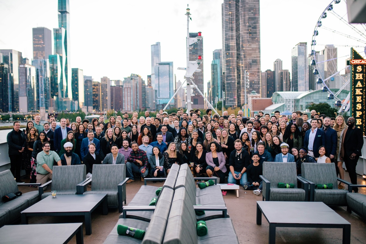 A large group of Vouch professionals pose for a group photo in front of the Chicago skyline. 