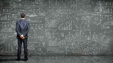 A man stands in front of a wall covered in scientific and mathematical equations.