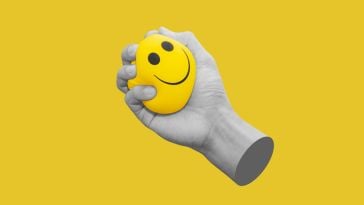 A hand gripping a yellow smiley-face stress ball over a yellow background.