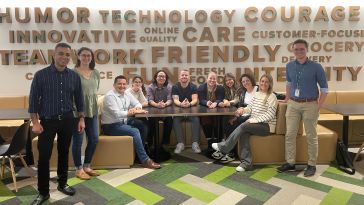 Group photo of Ahold Delhaize USA team members sitting in a booth with stylized word wall behind them. 